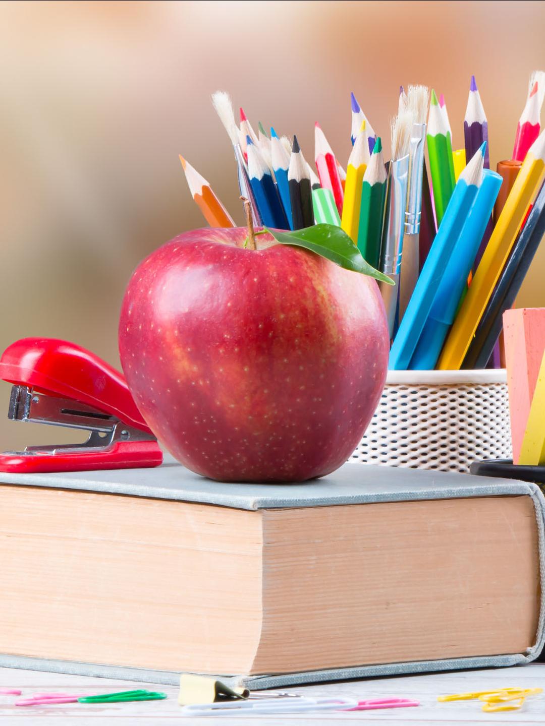 An apple on a text book next to school supplies