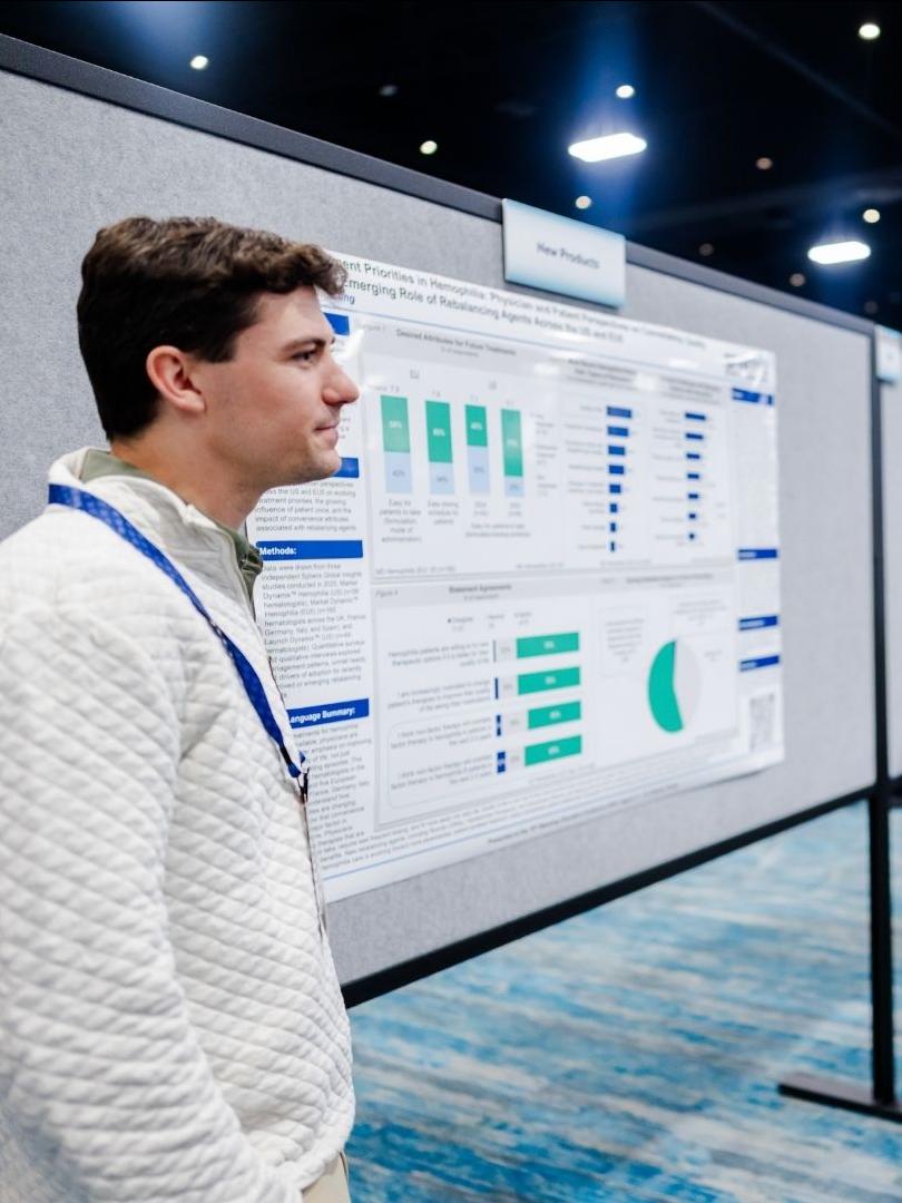 A man and a woman are standing in front of a research poster abstract in a large exhibit hall