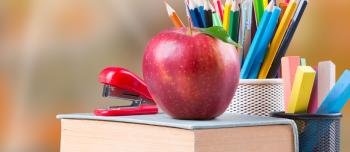 An apple on a text book next to school supplies An apple on a text book next to school supplies