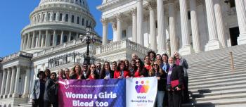 Women and girls with bleeding disorders standing on the steps of the capitol building in Washington DC, holding a banner that says "Women and girls bleed too"