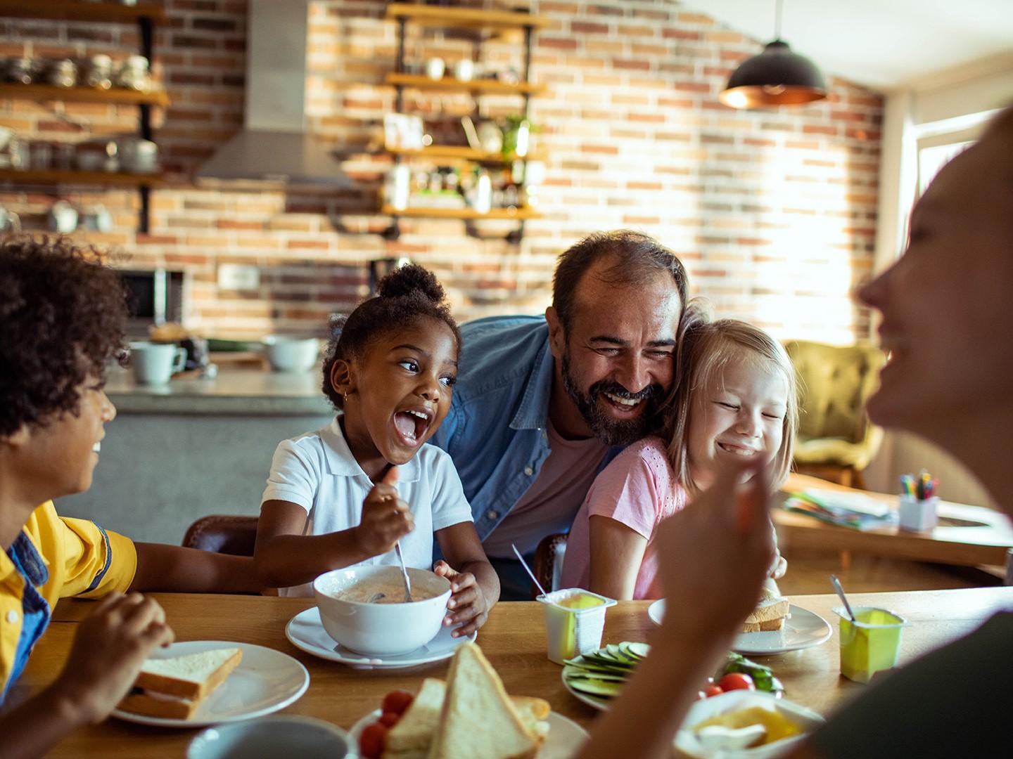 A man hugging his two kids at the dining room table