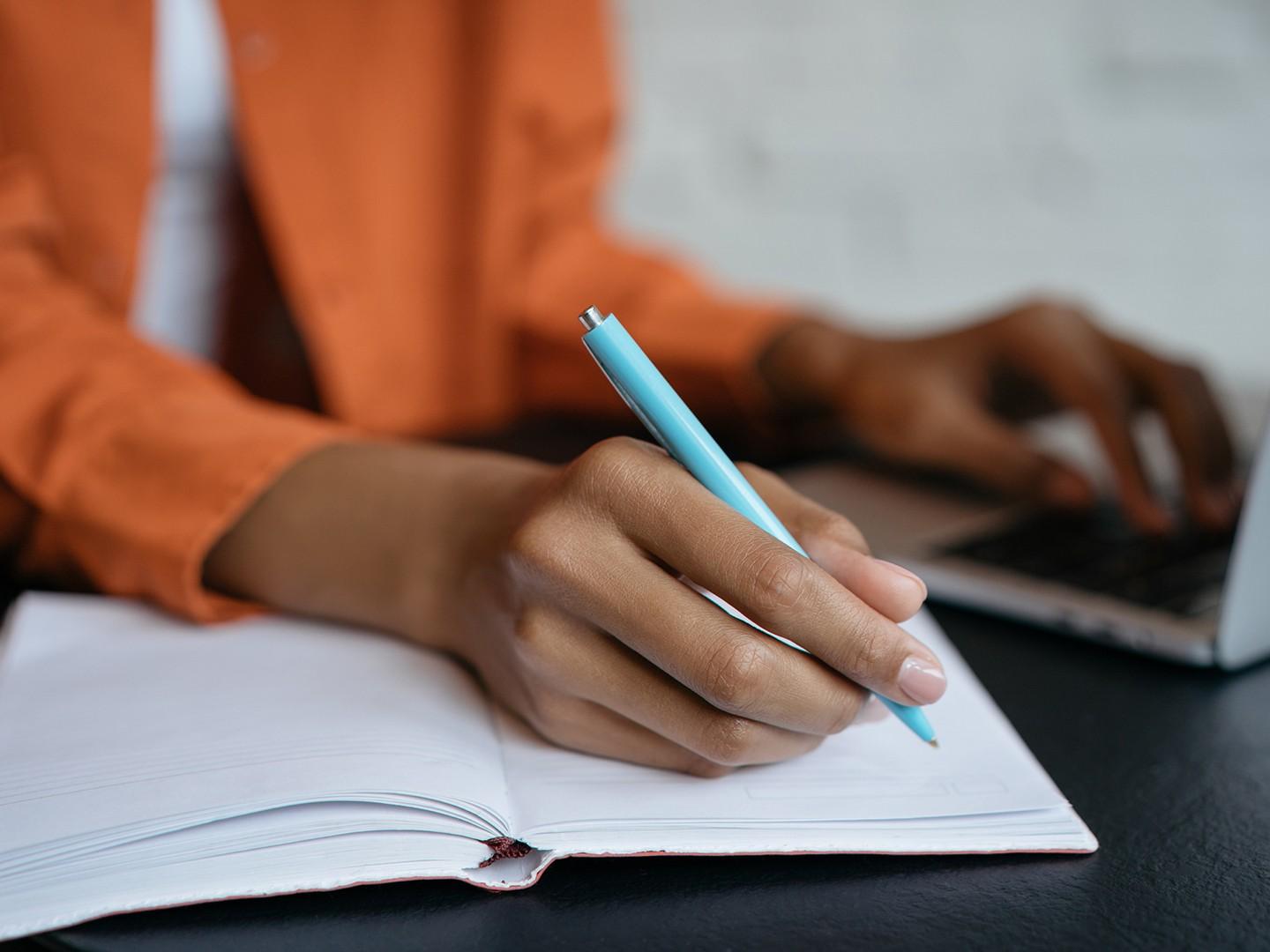 A person writing and using a laptop